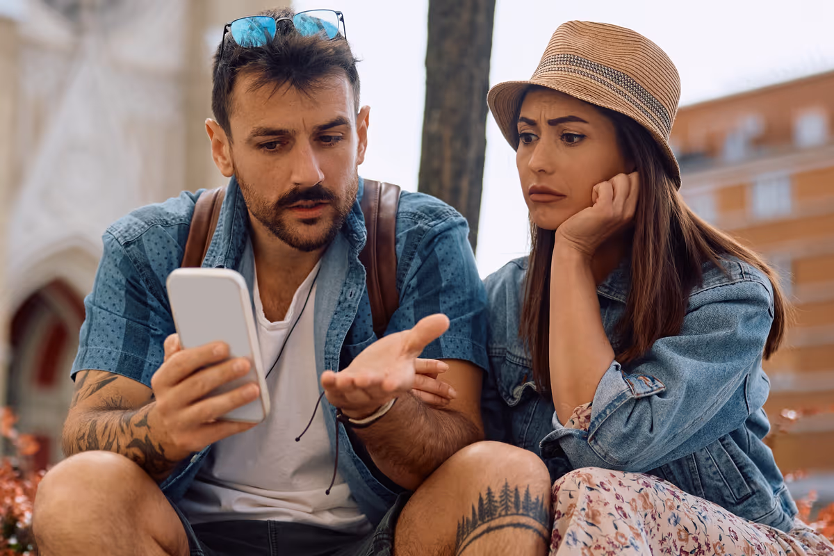Giovane coppia confusa guarda lo schermo di uno smartphone seduta all'aperto