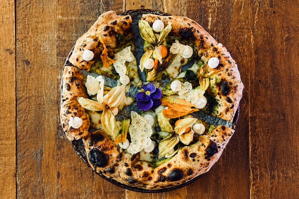 La pizza Luce d'estate, con crema di zucchine, fiori di zucca, mozzarella, ricotta, pesto di prezzemolo, germogli, physalis e chips di Grana Padano